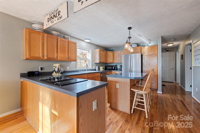 kitchen featuring stainless steel fridge, decorative light fixtures, black electric stovetop, a center island, and a breakfast bar