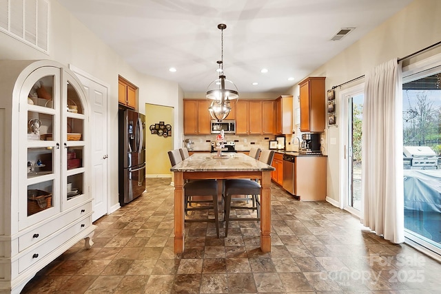 kitchen featuring pendant lighting, appliances with stainless steel finishes, light stone counters, tasteful backsplash, and a kitchen island