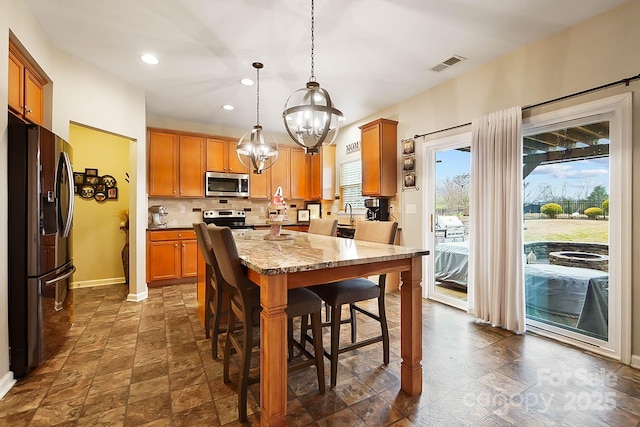 kitchen with light stone counters, decorative light fixtures, a chandelier, appliances with stainless steel finishes, and backsplash