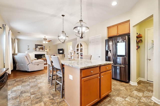 kitchen featuring light stone counters, decorative light fixtures, a center island, a kitchen breakfast bar, and stainless steel fridge