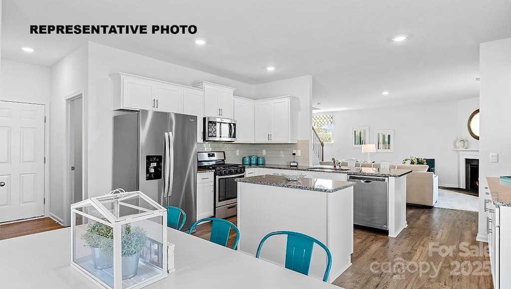 kitchen with stainless steel appliances, white cabinetry, a kitchen island, and light stone countertops