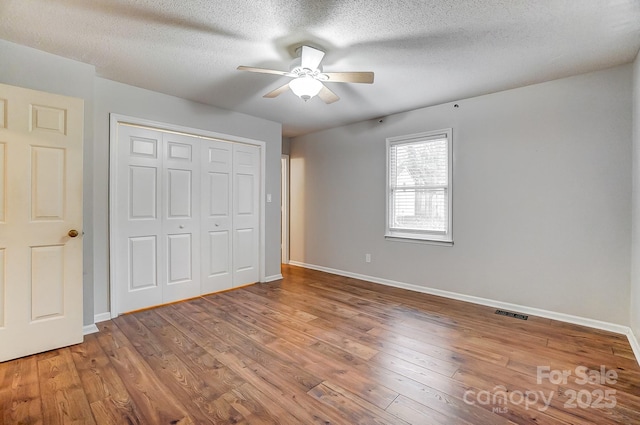 unfurnished bedroom featuring ceiling fan, wood-type flooring, a closet, and a textured ceiling