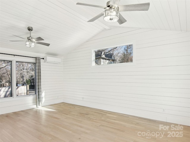 empty room with an AC wall unit, a healthy amount of sunlight, light hardwood / wood-style flooring, and vaulted ceiling