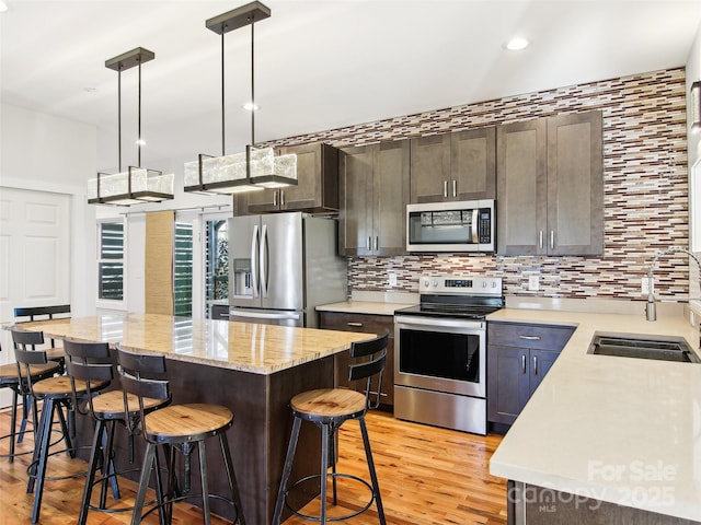 kitchen with hanging light fixtures, stainless steel appliances, dark brown cabinetry, a kitchen island, and sink