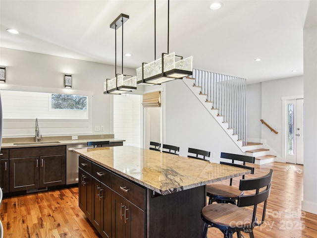 kitchen with sink, a kitchen island, light hardwood / wood-style floors, hanging light fixtures, and a breakfast bar area