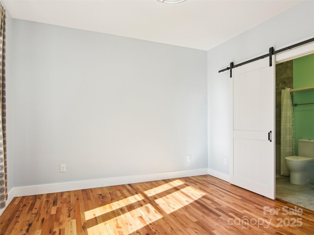 unfurnished bedroom with ensuite bathroom, wood-type flooring, and a barn door