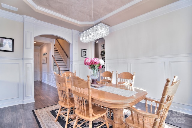 dining space with arched walkways, dark wood-style floors, a raised ceiling, and a decorative wall