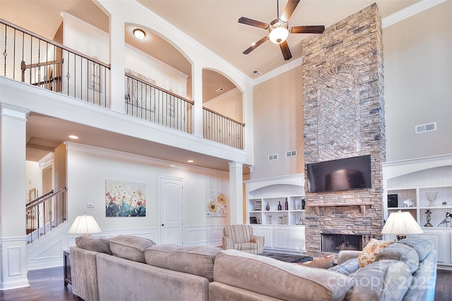 living area with built in shelves, ornamental molding, and a stone fireplace