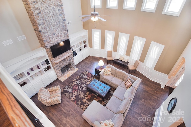 living room featuring dark wood-type flooring, a fireplace, ceiling fan, and a high ceiling