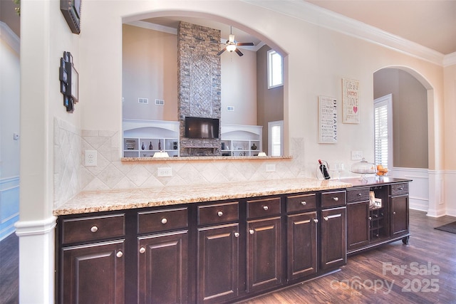 kitchen with ornamental molding, light stone counters, dark brown cabinets, and dark wood-style floors