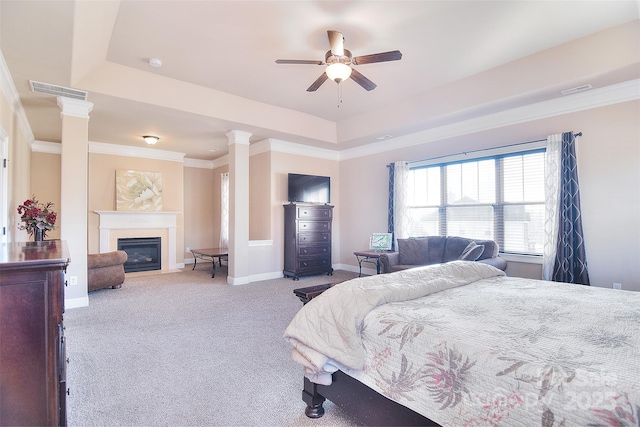 carpeted bedroom featuring a fireplace with flush hearth, baseboards, a raised ceiling, decorative columns, and crown molding