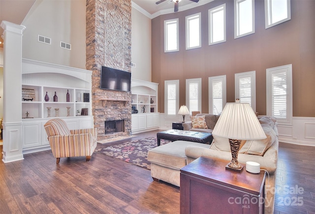 living room with dark wood-type flooring, ornamental molding, a stone fireplace, and a wealth of natural light