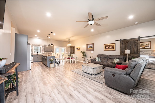 living room featuring ceiling fan, sink, a barn door, and light hardwood / wood-style floors