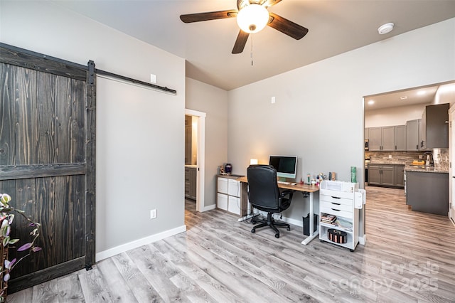 office space featuring ceiling fan, a barn door, and light hardwood / wood-style floors