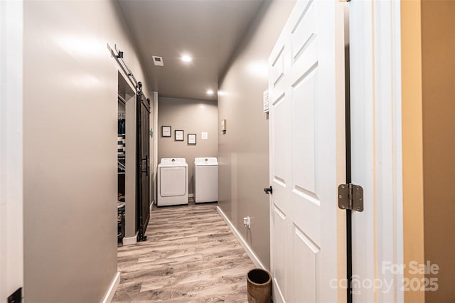 corridor featuring a barn door, washing machine and dryer, and light hardwood / wood-style flooring