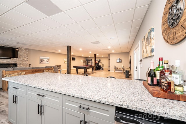 kitchen with light stone counters, a large fireplace, dishwasher, and a drop ceiling