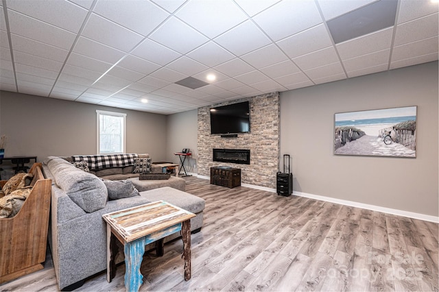 living room featuring a stone fireplace, hardwood / wood-style floors, and a drop ceiling