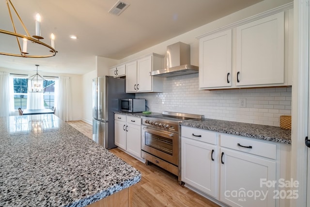 kitchen with white cabinetry, appliances with stainless steel finishes, wall chimney range hood, and decorative light fixtures