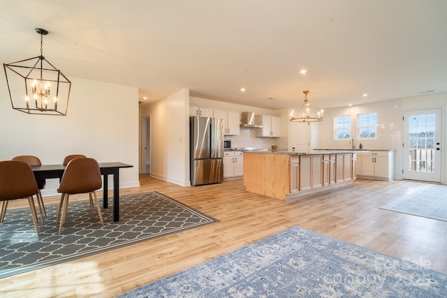 kitchen with wall chimney range hood, stainless steel refrigerator, a kitchen island, and decorative light fixtures