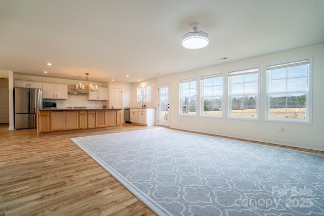 unfurnished living room with sink, an inviting chandelier, and light wood-type flooring