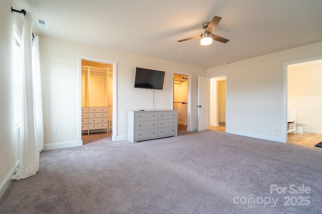 unfurnished bedroom featuring a closet, a walk in closet, ensuite bath, ceiling fan, and light colored carpet