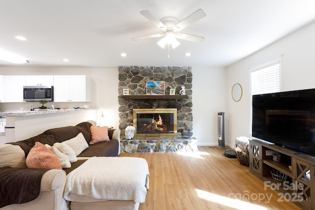 living room with a stone fireplace, light hardwood / wood-style flooring, and ceiling fan