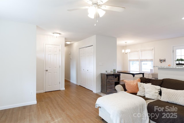 living room with ceiling fan with notable chandelier and light hardwood / wood-style flooring