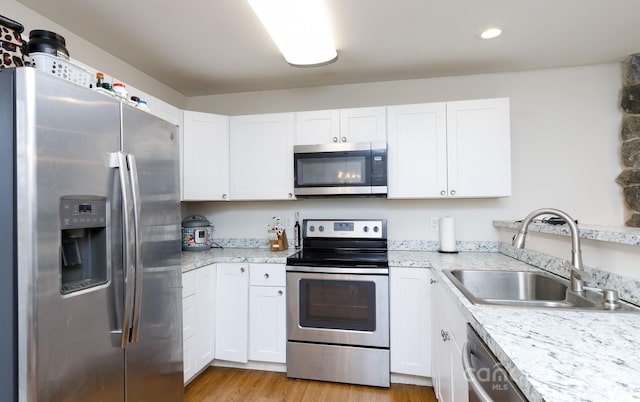 kitchen with sink, light hardwood / wood-style flooring, stainless steel appliances, light stone countertops, and white cabinets