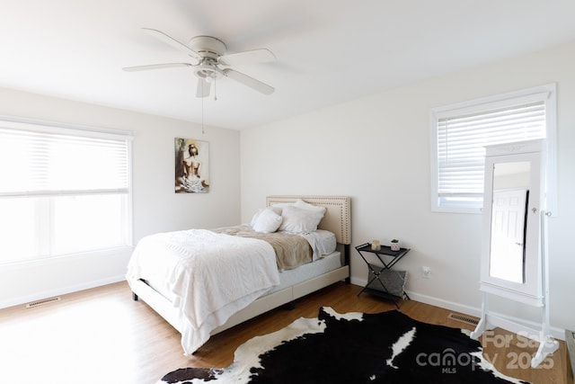 bedroom featuring multiple windows, wood-type flooring, and ceiling fan