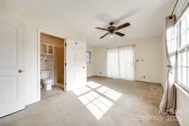 unfurnished bedroom featuring a walk in closet, light carpet, connected bathroom, and ceiling fan