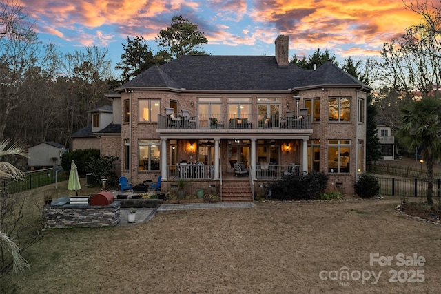 back house at dusk featuring a lawn, a patio, a balcony, and exterior kitchen