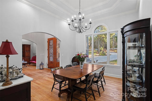 dining space with crown molding, a notable chandelier, light hardwood / wood-style floors, and a tray ceiling