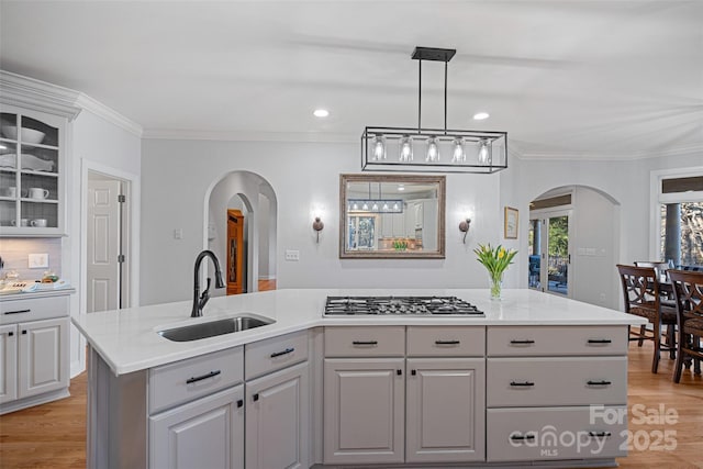 kitchen with sink, gray cabinetry, crown molding, an island with sink, and stainless steel gas stovetop