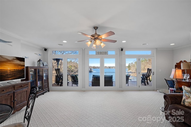 carpeted living room with ornamental molding, ceiling fan, and a water view