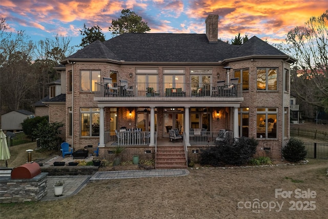 back house at dusk with a balcony, a porch, a yard, and a patio area