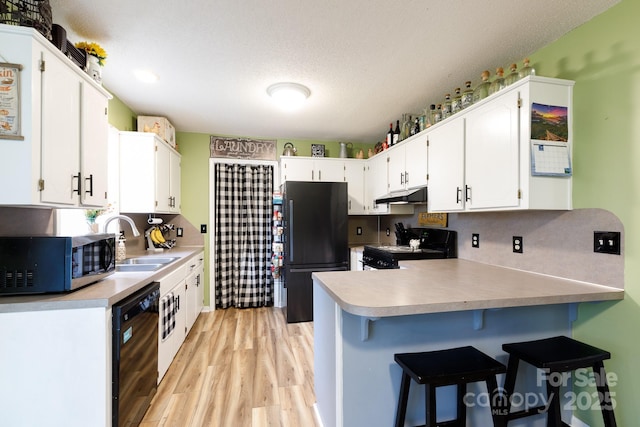 kitchen with white cabinetry, sink, a breakfast bar area, black appliances, and a textured ceiling