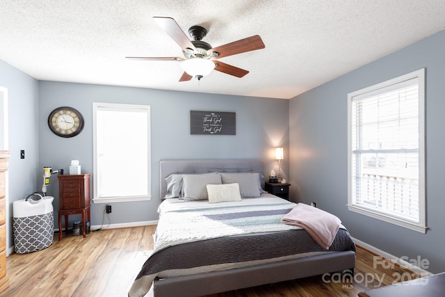 bedroom with ceiling fan, a textured ceiling, multiple windows, and light wood-type flooring