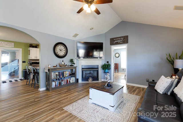 living area featuring a wealth of natural light, a fireplace, vaulted ceiling, and wood finished floors