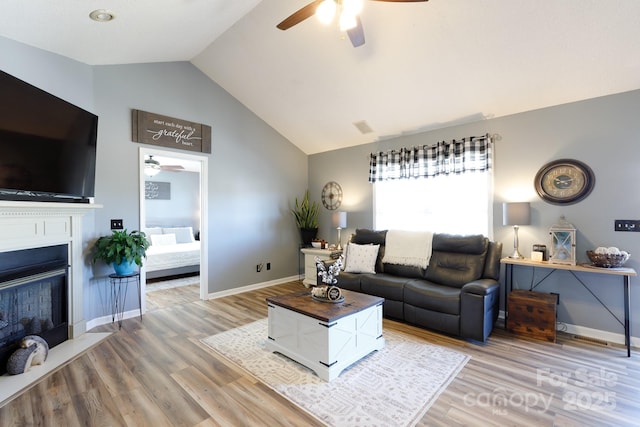 living room featuring light wood-type flooring, a fireplace, baseboards, and ceiling fan