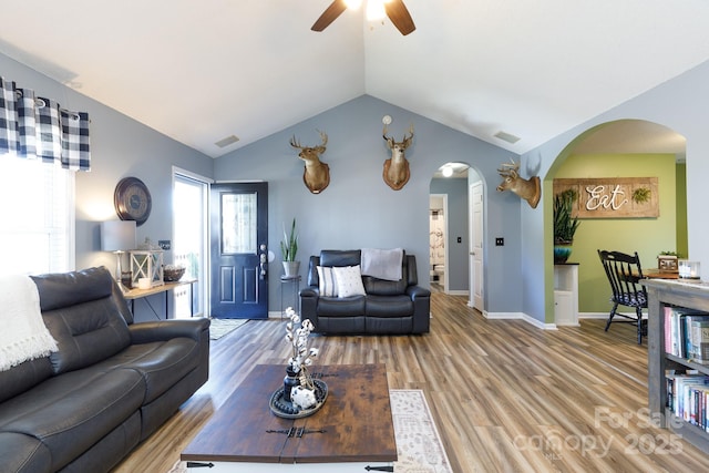 living room with arched walkways, visible vents, lofted ceiling, and light wood-style flooring