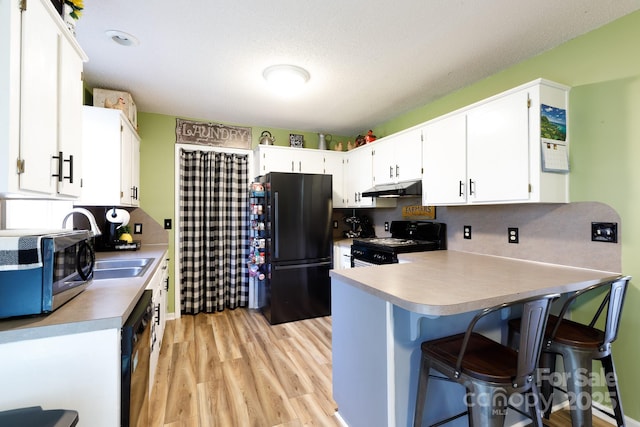 kitchen featuring light wood-style flooring, under cabinet range hood, a peninsula, white cabinets, and black appliances