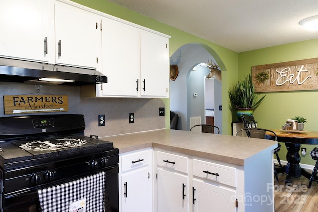 kitchen with arched walkways, white cabinets, a peninsula, black gas stove, and under cabinet range hood