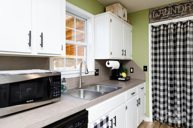 kitchen featuring light countertops, stainless steel microwave, a sink, and white cabinets