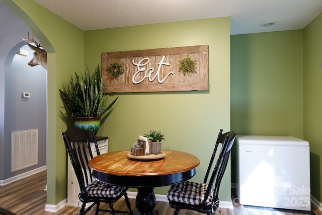 dining room featuring arched walkways, visible vents, baseboards, and wood finished floors