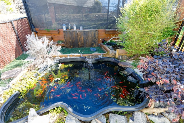 exterior space with a jacuzzi, fence, and a garden pond