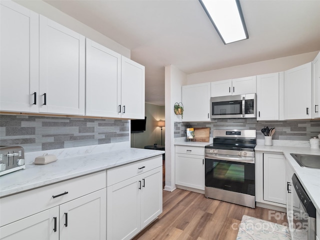 kitchen with white cabinetry, stainless steel appliances, light wood-type flooring, and backsplash