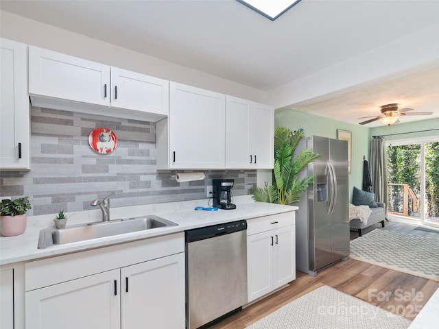 kitchen with appliances with stainless steel finishes, white cabinetry, sink, backsplash, and light hardwood / wood-style flooring