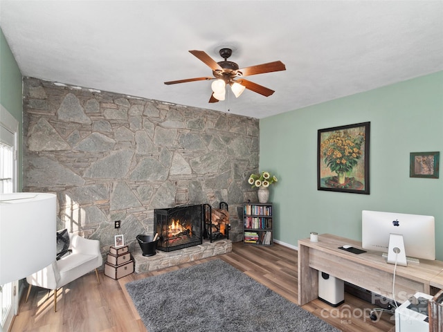 office area featuring hardwood / wood-style flooring, a stone fireplace, and ceiling fan