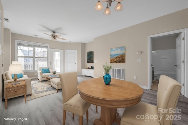 dining space featuring ceiling fan with notable chandelier and wood-type flooring