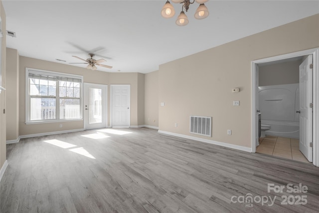 unfurnished living room with ceiling fan with notable chandelier and light hardwood / wood-style flooring